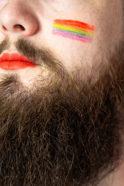 Young handsome bearded man with pride flag on his cheek, rainbow flag standing for LGBTQ, Gender right and sexual minority. Portrait — Stock Photo, Image