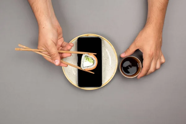 Online food delivery concept, sushi on phone's screen and chopsticks