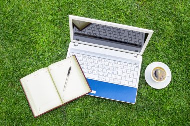 Beyaz dizüstü bilgisayar, dizüstü bilgisayar, kahve Kupası ve yerleştirilir üzerinde yeşil çim sahası kalem.