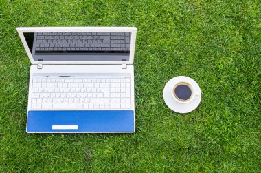 Laptop, kahve fincan beyaz ve yeşil çim sahası üzerinde yerleştirilen kalem.