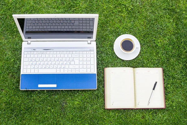 Beyaz dizüstü bilgisayar, dizüstü bilgisayar, kahve Kupası ve yerleştirilir üzerinde yeşil çim sahası kalem.