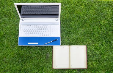 Beyaz Laptop, defter ve kalem yeşil çim sahada yer.
