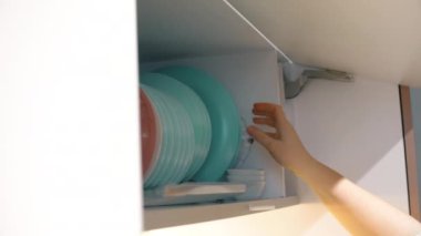 Female hand takes a plate from the kitchen cabinet. Woman take plate and close a kitchen shelf. Close up slow motion footage.