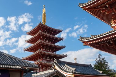 Tokyo 'daki Senso-ji Budist Tapınağı' ndaki geleneksel beş katlı Pagoda 'nın arka planında kırmızı oymalı çatı ve mavi gökyüzü var.. 