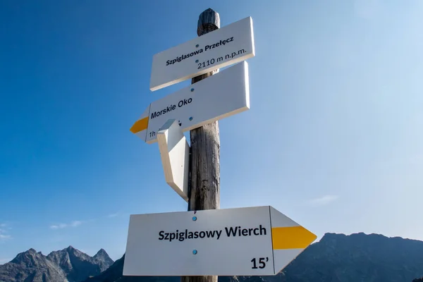 Mountain trail wooden directional sign in Tatra Mountains, pointing direction to Morskie Oko lake (Eye of the Sea) and Szpiglasowa Przelecz Pass, crystal blue sky background with mountain peaks.