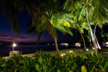 Romantic evening on the beach with dinner table on sand and illuminated palm trees around, Maldives.