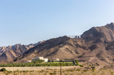 Hatta 'deki Hajar Dağları, tepenin üstünde Büyük Hollywood tarzı Hatta tabelası ile, Birleşik Arap Emirlikleri.