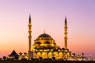 Yeni Şeriat Camii, Şeriat Emirliği 'nin en büyük camisi, Birleşik Arap Emirlikleri, pembe gökyüzü günbatımı ve akşam aydınlatmaları ile.