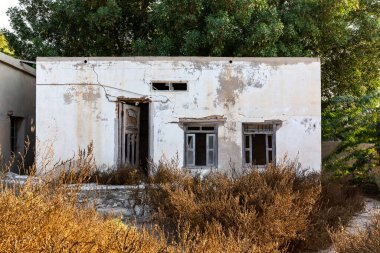 El Cezire El Hamra 'da, Birleşik Arap Emirlikleri' nin Ras El Khaimah kasabasında, pencereleri kırık, mavi pencere panjurları ve kapıları olan ihmal edilmiş bina cephesi..