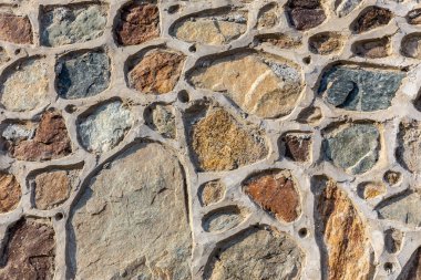 Colorful stony wall, multiple stones linked with cement, stone texture.