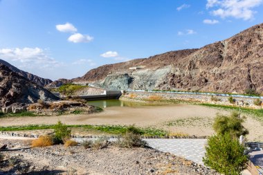Wadi Shawka Barajı, Hajar Dağları 'nda neredeyse boş bir baraj, Ras al Khaimah, Birleşik Arap Emirlikleri, arka planda kayalık dağlar ve kurumuş nehir yatağı..