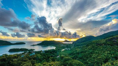Mahe Island coast high resolution drone panorama during sunset, with dramatic sky, clouds, lush tropical forest and small islands around.