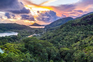 Mahe Island coast drone sunset landscape with dramatic pink sky, clouds, lush tropical forest and small islands around.