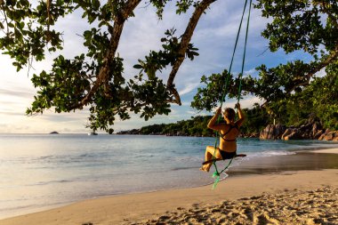 Anse Lazio plajındaki ağaçtan sarkan tahta salıncakta sallanan ve Praslin Adası, Seyşeller sahiline çarpan beyaz saçlı genç bir kadın..