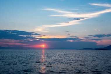 Yunanistan 'ın Marmari kentindeki Chersonisi Adası' ndaki Xero Körfezi 'nden görülen Akdeniz üzerindeki katman bulutlarıyla kırmızı ve mavi gün batımı.