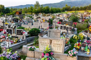 Milowka, Polonya, 08.07.2021. Geleneksel granit mezarlı, renkli suni çiçekler ve mumlarla süslenmiş Milowka köyü Beskid Dağları 'nın arka planında dağlar olan bir mezarlık..