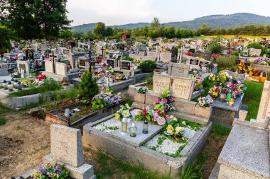 Milowka, Polonya, 08.07.2021. Geleneksel granit mezarlı, renkli suni çiçekler ve mumlarla süslenmiş Milowka köyü Beskid Dağları 'nın arka planında dağlar olan bir mezarlık..