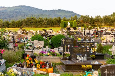 Milowka, Polonya, 08.07.2021. Geleneksel granit mezarlı, renkli suni çiçekler ve mumlarla süslenmiş Milowka köyü Beskid Dağları 'nın arka planında dağlar olan bir mezarlık..