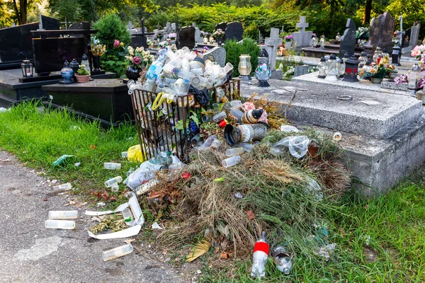 Trash container overflowing with used lamps, candles, artificial flowers and wreaths and other graves decorations in the Cemetery in Poland, plastic pollution in the cemetery after All Saints Day.