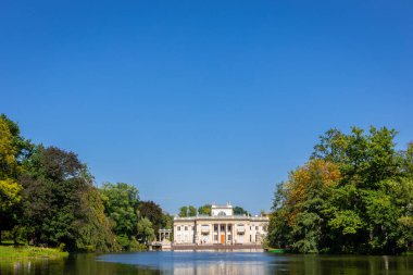 Varşova Kraliyet Hamamları Parkı 'ndaki Ada Sarayı (Lehçe: Palac Na Wyspie), önplanda göl manzarası, yeşil ağaçlar ve mavi gökyüzü, alçak ufuk, kopyalama alanı, Polonya.