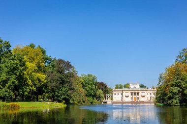 Varşova Kraliyet Hamamları Parkı 'ndaki Ada Sarayı (Lehçe: Palac Na Wyspie), önplanda göl manzarası, yeşil ağaçlar ve mavi gökyüzü, alçak ufuk, kopyalama alanı, Polonya.