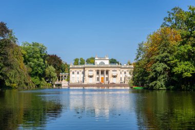 Varşova Kraliyet Hamamları Parkı 'ndaki Ada Sarayı (Lehçe: Palac Na Wyspie), önplanda göl, yeşil ağaçlar ve mavi gökyüzü, suda yansımalar, Polonya.
