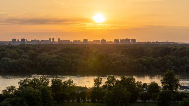 Tuna Nehri 'nin Belgrad, Sırbistan' daki Sava ile kavşağındaki gün batımı manzarası, yemyeşil ağaçlar ve Belgrad 'ın ufuk çizgisi, Belgrad Kalemegdan Park' ın Belgrad Kalesi 'ndeki manzarası.