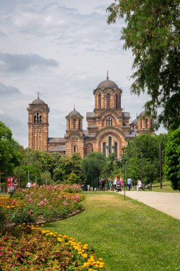 Belgrad, Sırbistan, 08.07.22. Yeşil yaz mevsiminde bir Sırp Ortodoks kilisesi olan St. Mark Kilisesi, çiçek açan bahçeleri ve yürüyen insanları olan Tasmajdan Parkı manzaralı..