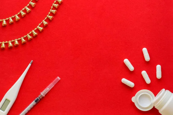Medical Christmas background. Pills, blister pack, syringe and thermometer on a red background. Flatly. Copy space.