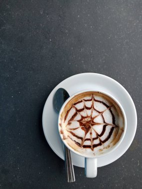 Gri taştan bir yüzeye yerleştirilmiş beyaz bir fincanda kahve sanatı..