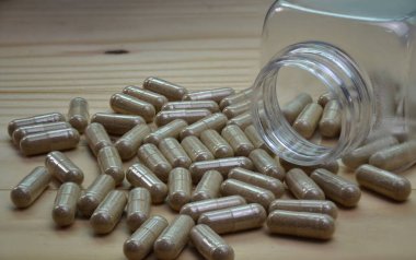 Zarif bitkisel toz içeren kapsüller. Tahta zemine tutunmak için kullanılan temiz bir plastik şişeden dökülmüş..