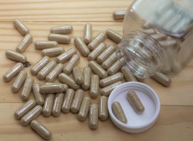 Zarif bitkisel toz içeren kapsüller. Tahta zemine tutunmak için kullanılan temiz bir plastik şişeden dökülmüş..