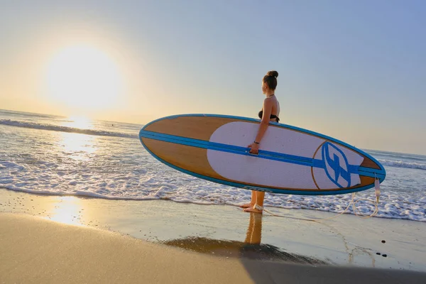 Jovem menina bonita em um maiô com uma prancha de surf ao amanhecer — Fotografia de Stock