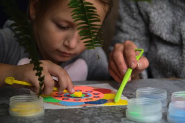 Renkli kumdan yapılmış bir mandala, kızların annesi.