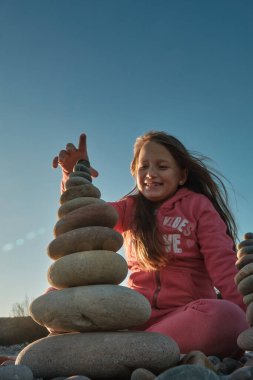 Bir kız kumsalda taşlardan bir piramit inşa ediyor.
