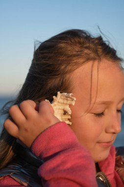 Bir kız sahilde deniz kabuğu dinler.