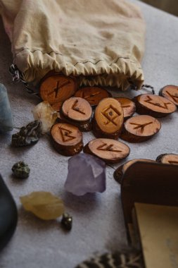 Masanın üzerinde rünler, bir kitap, bir büyüteç var.