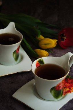 iki beyaz fincan çay ve sarı ve kırmızı laleler.