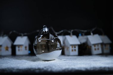 Karla kaplı evlerin arkaplanına karşı şeffaf Noel ağacı topu