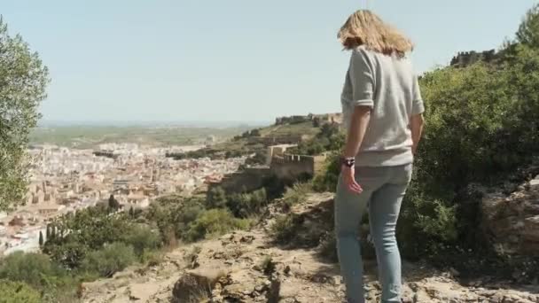 Una mujer joven mira desde la montaña en el pueblo — Vídeos de Stock