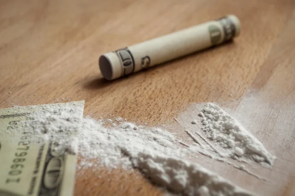 Auf einem Holztisch wurde weißes Pulver in der Nähe des Geldes verstreut, ein Geldschein wurde in ein Rohr gerollt — Stockbild Dollar und Kokain — Stockfoto