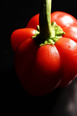 Siyah arka planda yeşil kuyruklu kırmızı tatlı biber. Loş ışıklar. Kapat.