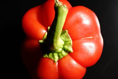 Siyah arka planda yeşil kuyruklu kırmızı tatlı biber. Loş ışıklar. Kapat.