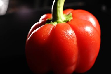Siyah arka planda yeşil kuyruklu kırmızı tatlı biber. Loş ışıklar. Kapat.