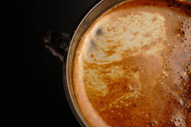 Şeffaf bir fincanda kahve. Işık loştu. Siyah bir arkaplanda.