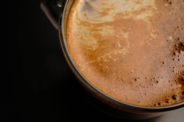 Şeffaf bir fincanda kahve. Işık loştu. Siyah bir arkaplanda.