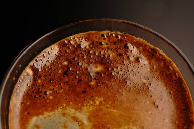 Şeffaf bir fincanda kahve. Işık loştu. Siyah bir arkaplanda.