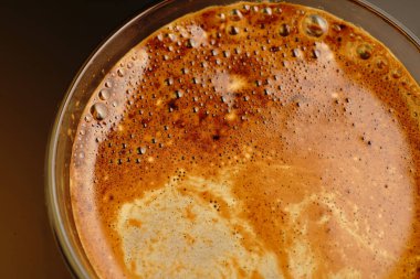 Şeffaf bir fincanda kahve. Işık loştu. Siyah bir arkaplanda.