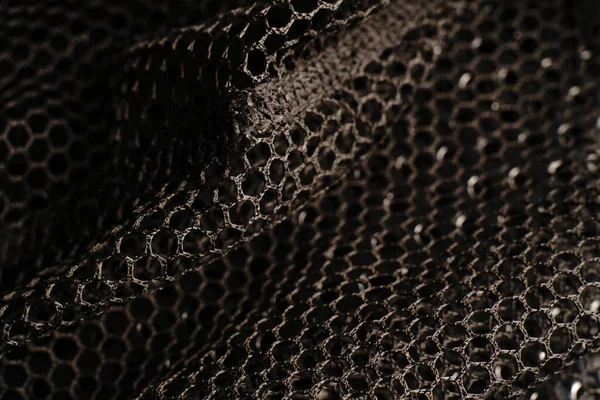 Black texture. A black net is placed on a black perforated metal table. The light glares.