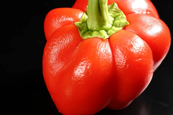 Siyah arka planda yeşil kuyruklu kırmızı tatlı biber. Loş ışıklar. Kapat.